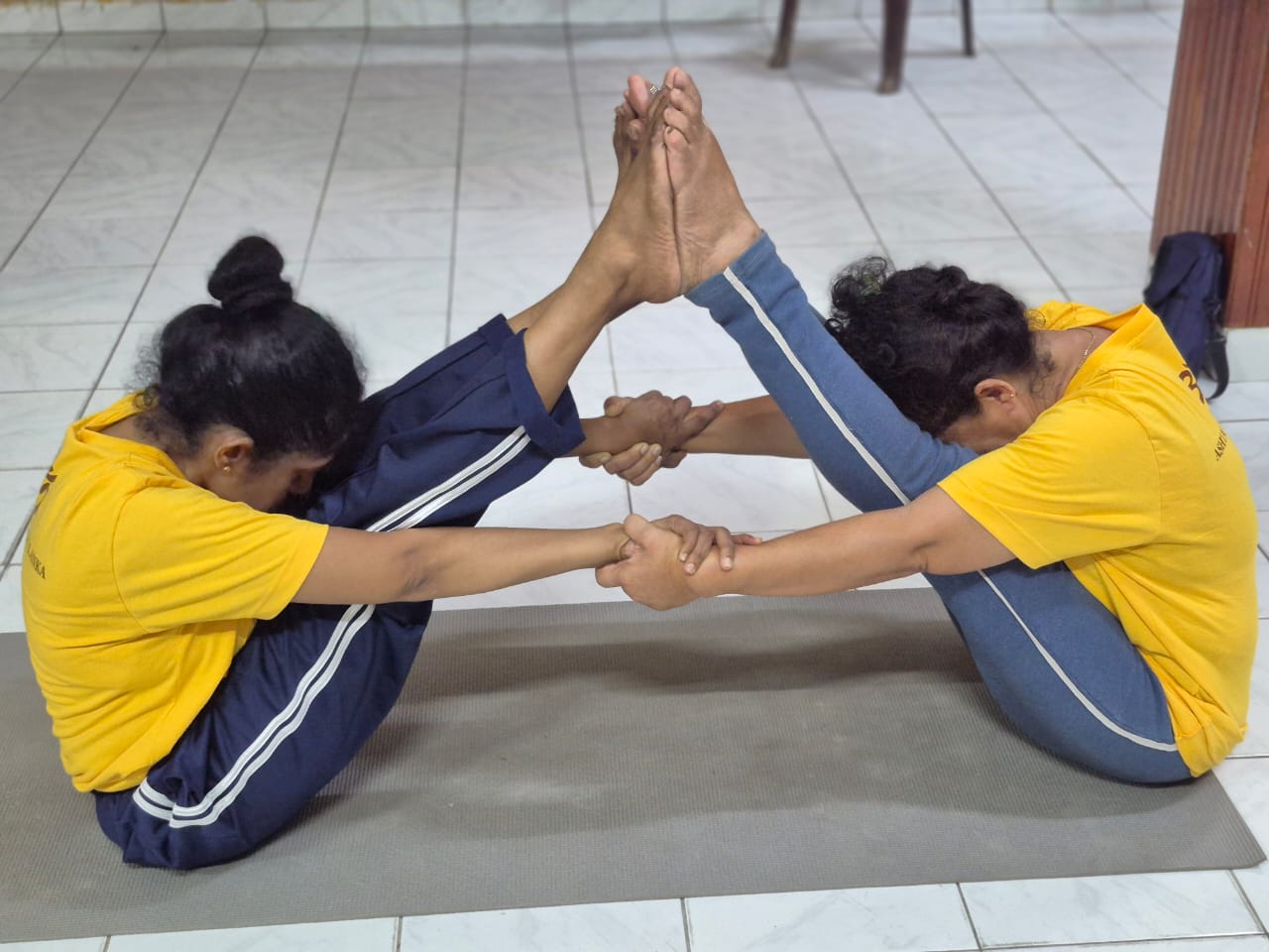 Two students in partner boat pose on a shared mat